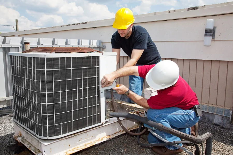 Two technicians in hard hats servicing a commercial rooftop HVAC condenser